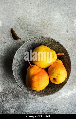 From above ceramic bowl with organic pears fruit on concrete surface Stock Photo