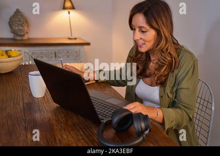 Woman browsing data on laptop while sitting at table and working remotely from home Stock Photo