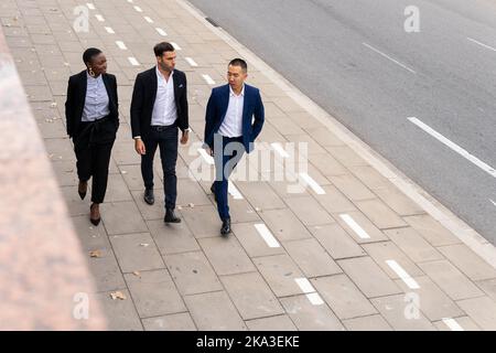 From above multiracial coworkers in formal outfits walking along paved sidewalk and talking with each other Stock Photo