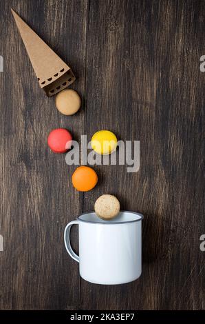 From above colorful French macaroons with various fillings falling from paper cone into a mug on wooden table Stock Photo