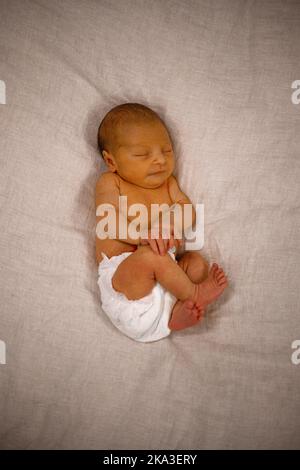 Top view of adorable infant baby in diaper lying on soft blanket with crossed legs and arms while sleeping Stock Photo