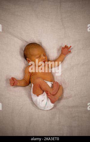 Top view of adorable infant baby in diaper lying on soft blanket with crossed legs while sleeping Stock Photo