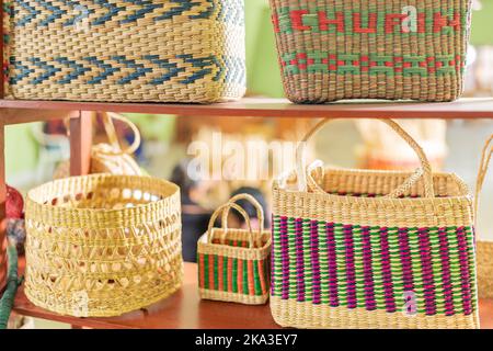 Many colorful wicker baskets placed on shelves on blurred background of sunlit workshop in daytime Stock Photo