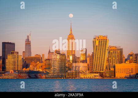 Modern skyscrapers and Empire State Building located on shore of New York Bay against sundown sky with moon in Manhattan Stock Photo