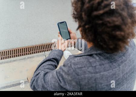 From above African American male tourist in casual clothes sitting on steps and browsing smartphone Stock Photo
