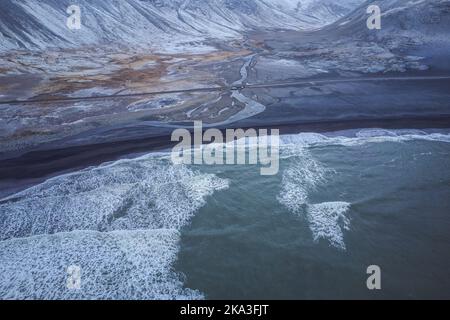 Aerial view of uneven coast of dark sea covered with white snow on cold winter day in Iceland Stock Photo