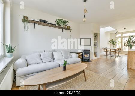 Comfortable sofa with cushions and small round coffee table in spacious light living room with soft rug on wooden floor and white walls near fireplace Stock Photo