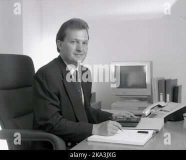 1991, historical, a suited male business executive sitting at his desk ...