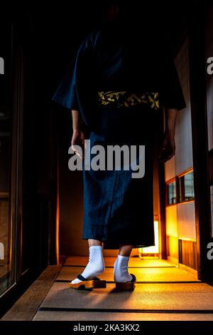 Unrecognizable man in Japanese kimono walking with geta socks and tabi shoes by shoji sliding paper doors at night and tatami mat vertical view in tra Stock Photo