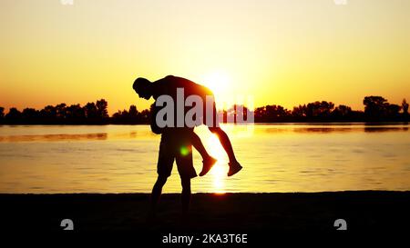 Two dark male figures, at sunrise, against the light, boxing, fighting in sparring, training in a pair of techniques of strikes. On sandy beach, in cargo port, near water, in summer. High quality photo Stock Photo
