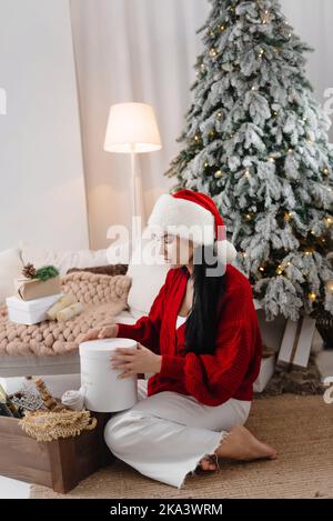 Happy young woman sitting in living room, unpacking cardboard box, shopping online for Christmas, smiling excited millennial girl opens cardboard Stock Photo