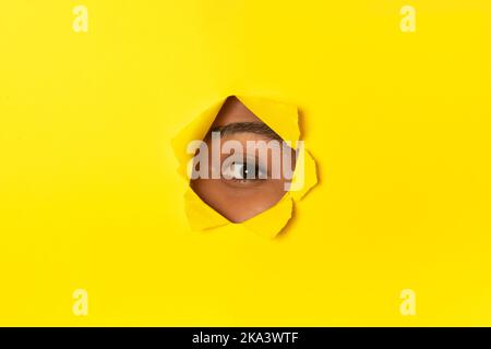Curious African Woman Peeking Through Hole In Torn Yellow Paper Stock Photo