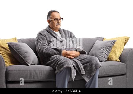 Pensive mature man wearing a bathrobe and sitting on a gray sofa isolated on white background Stock Photo