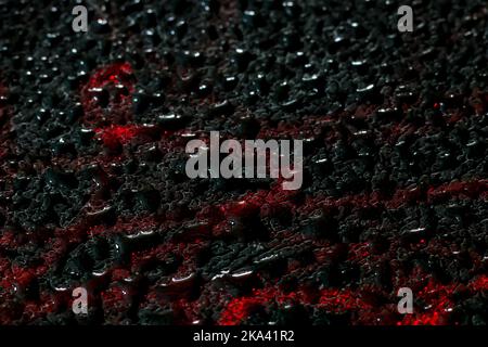 Water droplets afiery red glow on close up of black leather like material Stock Photo