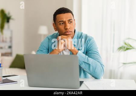 Pensive serious young african american guy with laptop working, freelancing remotely, making business decision Stock Photo