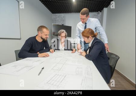 Four colleagues are discussing blueprints in a conference room in an office. Brainstorming of engineers and architects. Stock Photo