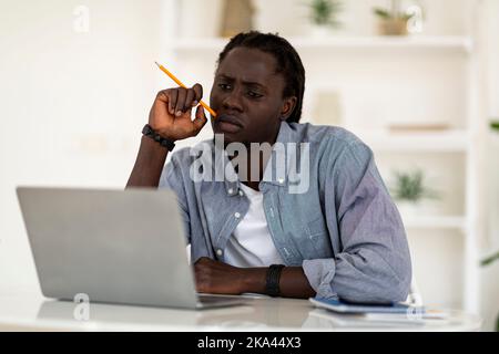 Thoughtful Young African American Man Holding Pencil And Looking At Laptop Screen Stock Photo