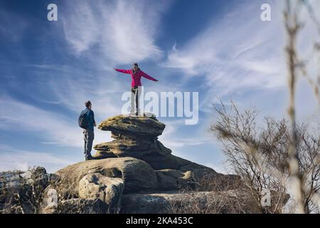 A woman stands with her arms outstretched while she balances on a rock formation, Brimham Rocks, Nidderdale, Harrogate, North Yorkshire, England. UK. Stock Photo