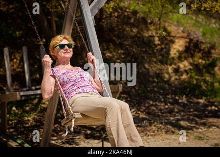 Senior woman joyfully swinging on a swing and having fan Stock Photo