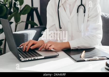 Close up of unknown female doctor in white coat lab with stethoscope typing at laptop computer, patient card, illness history. Female therapist physic Stock Photo