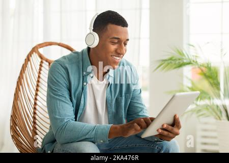 Smiling young african american guy in wireless headphones chatting, searching, surfing in internet Stock Photo
