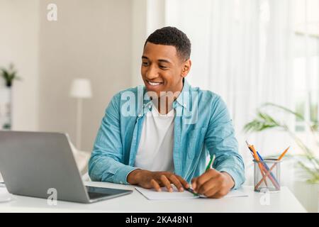 Glad handsome young african american man manager in casual use computer for work, study, making notes Stock Photo