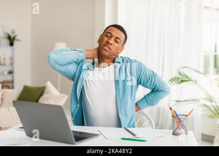 Sad young african american man use computer for study, work, suffering from fatigue and back, neck pain Stock Photo