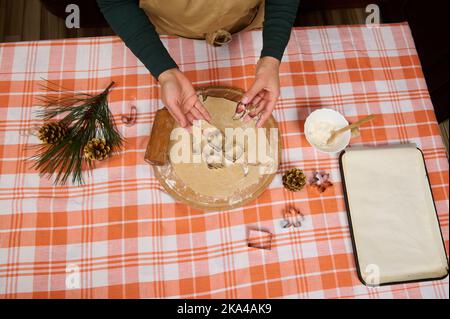 Directly above housewife's hands holding an angel wings shaped mold from gingerbread dough. Making cookies for Christmas Stock Photo