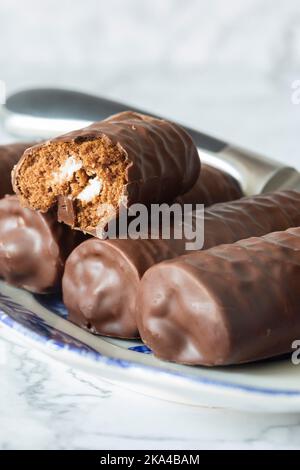 Individual chocolate sponge rolls on a patterned blue and white dish with a serving knife. On a white marble background Stock Photo