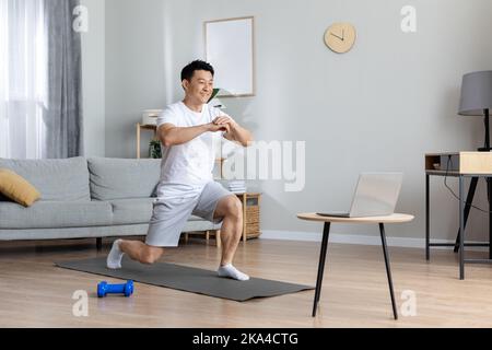 Motivated asian man exercising at home, using laptop Stock Photo