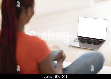 Black Woman Using Laptop With White Screen And Drinking Coffee At Home Stock Photo