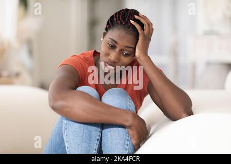 Portrait Of Depressed Young Black Woman Sitting On Couch At Home Stock Photo