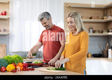 Happy middle aged spouses cooking and having conversation Stock Photo