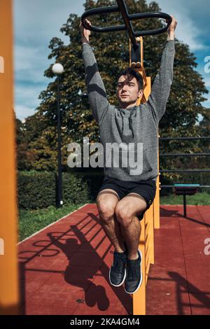 Young man bodybuilder exercising pulling up his legs during his workout in a modern calisthenics street workout park. Man wearing sportswear Stock Photo
