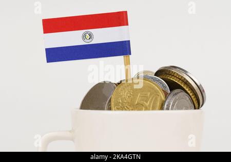 The flag of Paraguay sticks out from a cup with coins. Economy and business concept. close-up Stock Photo