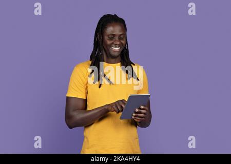 Happy stylish black guy using digital tablet on purple Stock Photo
