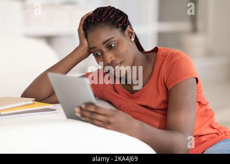 Young Black Woman Using Digital Tablet While Sitting At Desk At Home Stock Photo
