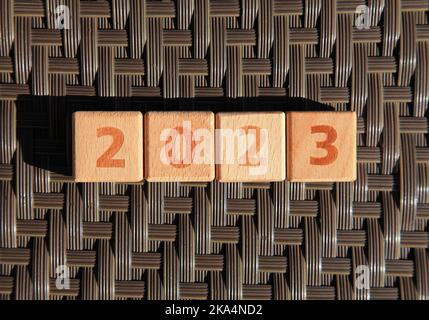 Inscription 2023. Wooden square cubes and numbers on plastic wicker surface means coming New Year Eve. Christmas, holidays and celebration concept Stock Photo