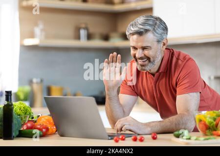 Cheerful man cooking at home, having video call, using laptop Stock Photo