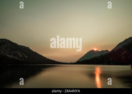 Toxaway Lake, an alpine lake in Idaho’s Sawtooth Wilderness seen on a summer day at dawn, with the sun rising over the mountains. Stock Photo