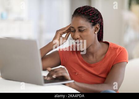 Portrait Of Stressed Young Black Freelancer Lady Having Headache While Using Laptop Stock Photo