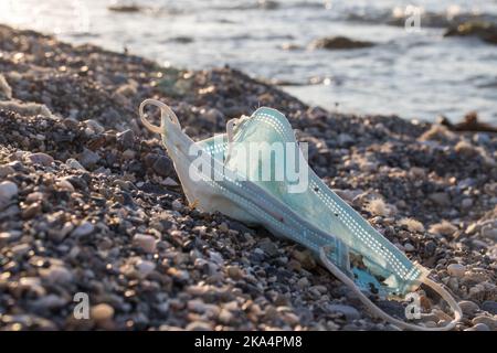 Discarded single -use face mask. Medical face mask on a beach. Stock Photo