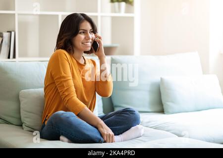 Young Arab Woman Talking On Cellphone While Resting On Couch At Home Stock Photo