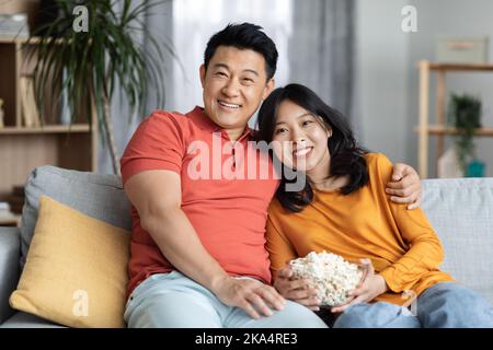 Relaxed korean spouses sitting on sofa, watching movie together Stock Photo