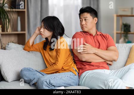 Upset asian couple sitting on couch at home Stock Photo