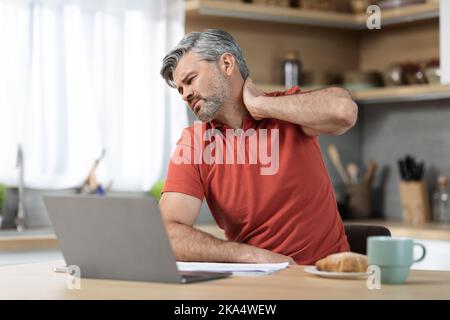 Tired man sitting in front of laptop, touching neck Stock Photo
