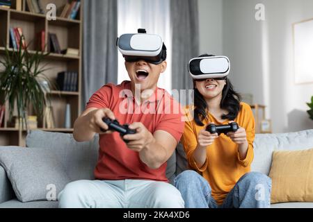 Happy korean couple playing video games at home, using headset Stock Photo