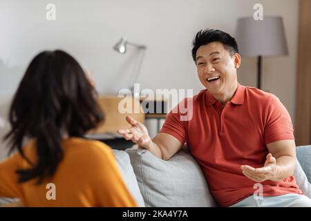 Positive asian man having conversation with woman, home interior Stock Photo