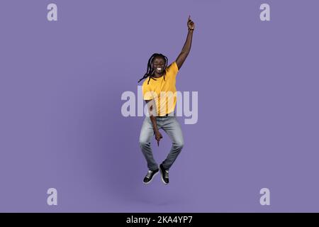Joyful african american guy jumping over purple background Stock Photo