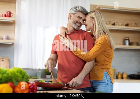 Romantic spouses bonding while preparing meal together at home Stock Photo